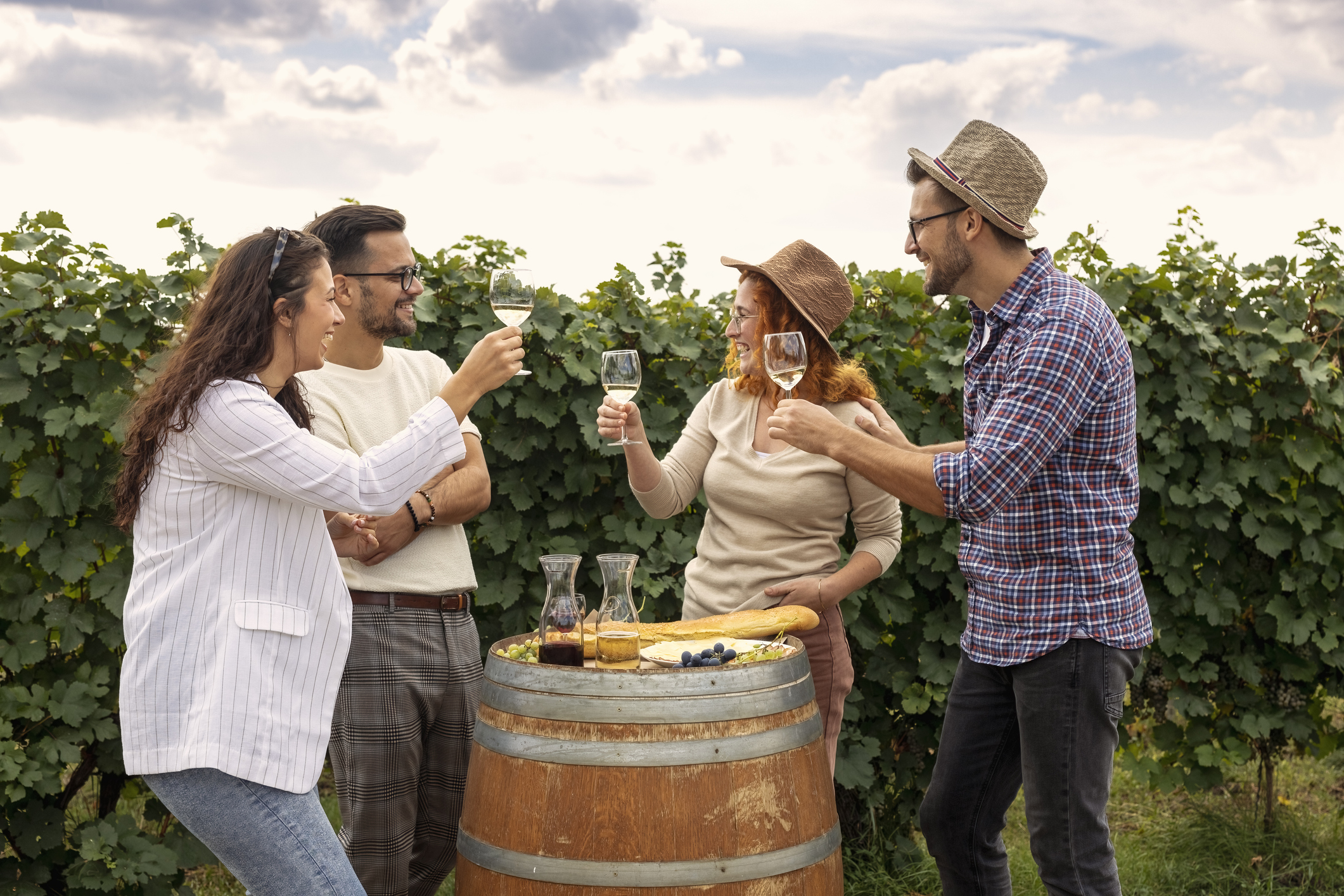 Four friends standing in a vineyard with glasses of red and white wine, drinking, relaxing, and talking to each other at a winery in Sonoma County.