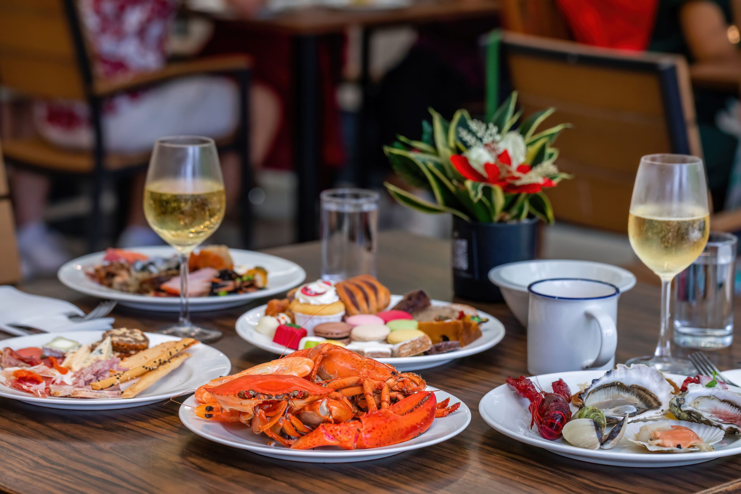 Fine dining table in a luxury restaurant in Monterey, CA, featuring steamed red crab, lobster, assorted gourmet seafood dishes, desserts, sweets, and champagne arranged elegantly on the table.