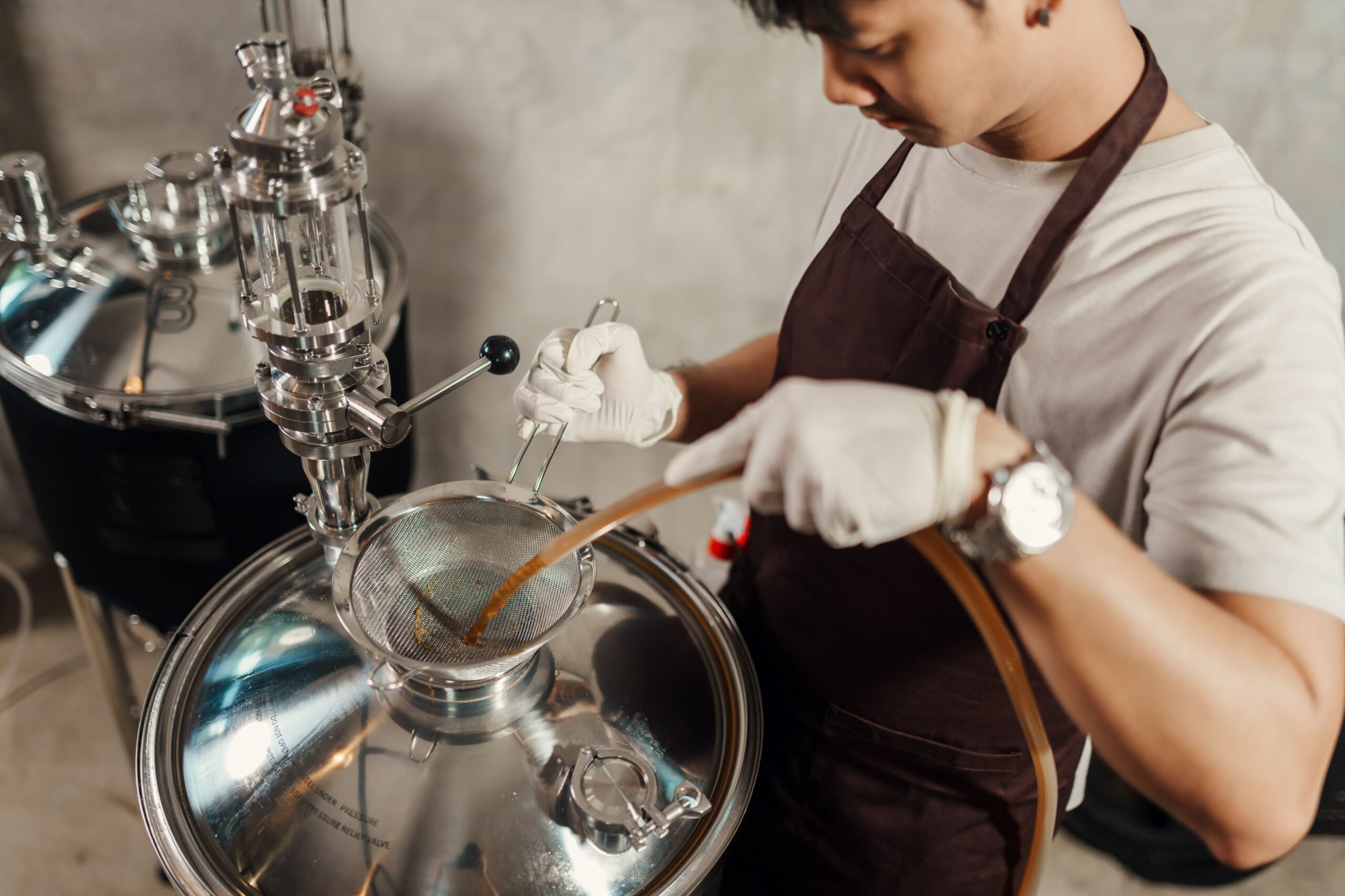 Top view of a craft brewer carefully transferring brewed wort after cooling down into a stainless steel fermenter using a sanitized hose and strainer.
