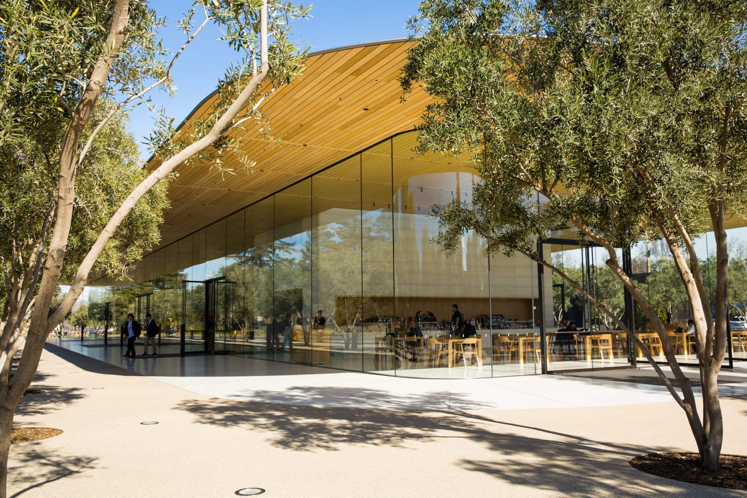 The Apple Visitor Center in San Jose, California with a modern glass and wood building designed by Norman Foster, featuring a cafeteria and shop next to the iconic Apple “Spaceship” Campus.